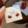 Deep red persimmon studs with gold leaf accents on a white display card - Red Persimmon Style (ZCM4)