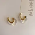 Detail of C-shaped resin earrings with gold metal core and wavy minimalist design - Transparent Irregular Style