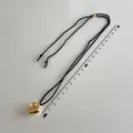 Detailed close-up of a gold heart pendant on a black woven cord with measuring ruler - Large Gold Heart Pendant Black Rope Style (B-293)