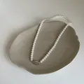 Gros plan du collier élégant en perles de verre blanches avec pendentif argenté sur plateau - Taille 5 Plaqué Or