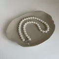 Gros plan d'un collier de perles blanches avec fermoir argenté sur plateau céramique - Taille 8 Plaqué Or