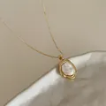 Dettaglio del ciondolo con perla barocca e cornice dorata ondulata su collana fine - Oro