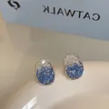 Macro shot of oval blue gradient crystal stud earrings with polished silver metal edges - Irregular Crystal Style