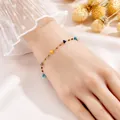 Elegantes Goldarmband mit bunten Edelsteinen, getragen am Handgelenk auf rosa Seide - Quadratische Bunte Stein Armband (5451)