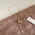 Detail of a vintage golden bead necklace with bow pendant and a dangling white pearl - Gold