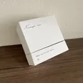Détail d'un coffret cadeau bijoux minimaliste en papier texturé blanc sur bois sombre - Boîte cadeau / 8x8cm