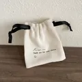 Vue détaillée d'une pochette à bijoux crème avec ruban noir et texte de remerciement - Sac de rangement / 8x8cm