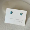 Nahaufnahme bunter Schmetterlings-Ohrstecker auf einer weißen Präsentationskarte - Schmetterlings-Stil / Cyan