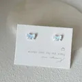 Close-up of iridescent butterfly stud earrings on a white elegant presentation card - Bow Shape / White