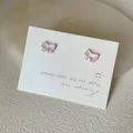 Detailaufnahme der schillernden Schmetterlingsohrstecker auf einer strukturierten Karte - Schleifenform / Rosa