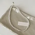 Close-up of pearl necklace with matte silver curved bar on a ceramic tray - Pearl Necklace / Gold