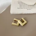 Detailopname van matgouden vierkante oorbellen met geborstelde metaaltextuur en smiley - Goud