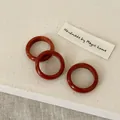 Detailed view of three minimalist dark reddish agate rings on textured beige fabric - Red Jasper