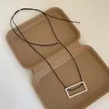 Close-up of a brushed silver rectangular pendant on a black cord necklace in a gift box - Square Necklace