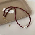 Macro shot of dark red beaded necklace featuring a white pearl and gold metal clasp detail - Red Gold Plated