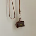 Detail of a dark brown vintage leather pouch with metal snap button and woven lanyard - Brown
