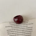 Close-up of a glossy burgundy resin ring with a thick curved design on vintage paper - Ring (3095)