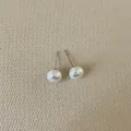 Detail of round pearl stud earrings with metallic sheen on beige textured background - Hemispherical Pearl / Mini Size (8mm)