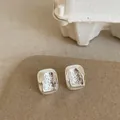 Minimalistische silberne Ohrringe mit strukturierter Flüssigmetall-Optik auf Karte - Quadratische Ohrstecker