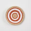 Detailed close-up of a bohemian woven seagrass wall plate with concentric orange patterns - A16