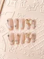 Dettaglio di unghie finte fatte a mano con smalto nude cat-eye e decori a farfalla dorata - XS