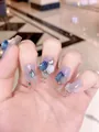 Dettaglio di unghie finte lunghe con strass blu, rose 3D e sfumatura di colore viola - XS