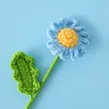 Gros plan d'une marguerite crochetée bleue avec cœur jaune et feuilles tricotées - Bleu ciel