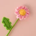 Handmade crochet daisy flower with pink petals and green leaf on a pastel pink background - Pink