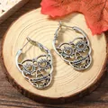 Gothic skull hoop earrings with heart-shaped eyes on natural wood background - Antique Silver