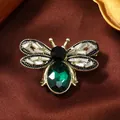 Detailaufnahme der goldenen Bienenbrosche mit grünem Edelstein und Kristallflügeln - Pfauengrün