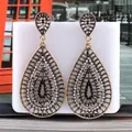 Macro view of vintage hollow teardrop earrings with crystals on a white display - White Antique KC Gold