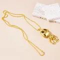 Detail of gold-colored round bead chain with cute skull robot pendant on beige background - X823