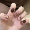 Detalle de uñas postizas cortas y redondas con diseño de leopardo y lazo marrón - M