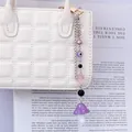 Detail of purple mushroom and evil eye charm pendant hanging on a white quilted bag - Purple
