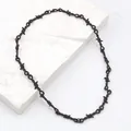 Detalle de collar punk negro mate estilo alambre de espino sobre podio de mármol - Collar Espinas Negro Armas