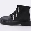 Detalle de botas de cuero negro con cordones y creativos colgantes metálicos de zapatos plateados - Colgante de Zapatillas
