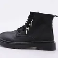 Detalle de botas militares negras mates con colgantes metálicos plateados en los cordones - Colgante de Cono