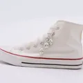Detalle de tres dijes de calavera plateados con cierres de langosta en zapatillas blancas - Colgante de Calavera