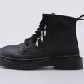 Detalle de botas de plataforma negras con colgantes metálicos únicos en forma de diente - Colgante de Diente