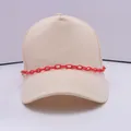 Detail einer cremefarbenen Baseballkappe mit einer dekorativen hellroten Acrylkette - Rot