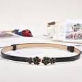 Women's black skinny belt with elegant gold-edged black flower buckle and glossy finish - Gold Four-Petal Buckle / Black