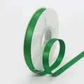 Green satin ribbon with gold glitter on a white spool for luxury gift packaging - Green