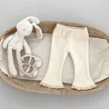 Close-up of baby ribbed knit flare pants with delicate lace trim at the hem and waistband - 73cm / Off White