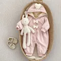 Detail of pink hooded baby romper with white bows and plush rabbit in a woven basket - Pink / 66cm