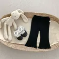 Detail of baby flared leggings featuring lettuce edge hem and size tag in a woven basket - 73 / Black