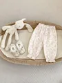 Flat lay of baby floral pants and lace shoes in a woven basket with a plush rabbit - 73 / Bottoms / Beige And Pink Floral