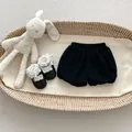 Flat lay of baby girl black bloomers and lace-trimmed shoes in a woven basket - Bloomer Shorts / 66cm