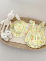 Detailed overhead view of floral baby bodysuit with matching sun hat in a woven basket - Yellow / 66cm