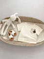 Flat lay of baby cotton T-shirt with cartoon rabbit print and white sandals in cradle - Apricot Rabbit