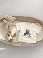 Detail of baby summer outfit with checkered bear t-shirt and white leather sandals - 66CM / Apricot